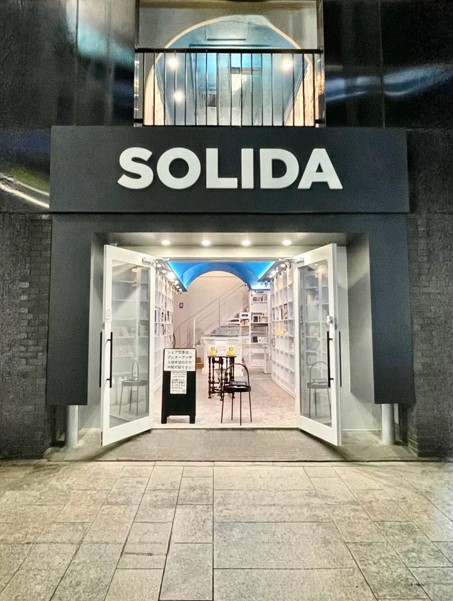 夜間に看板が見え、ドアが開いているSOLIDAの入口